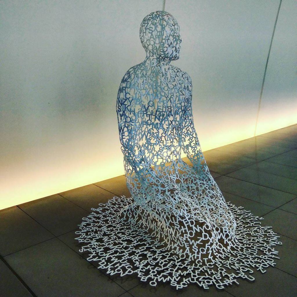 Letter-form sculpture of a seated human figure at Heydar Aliyev Center, backlit against a modern white wall